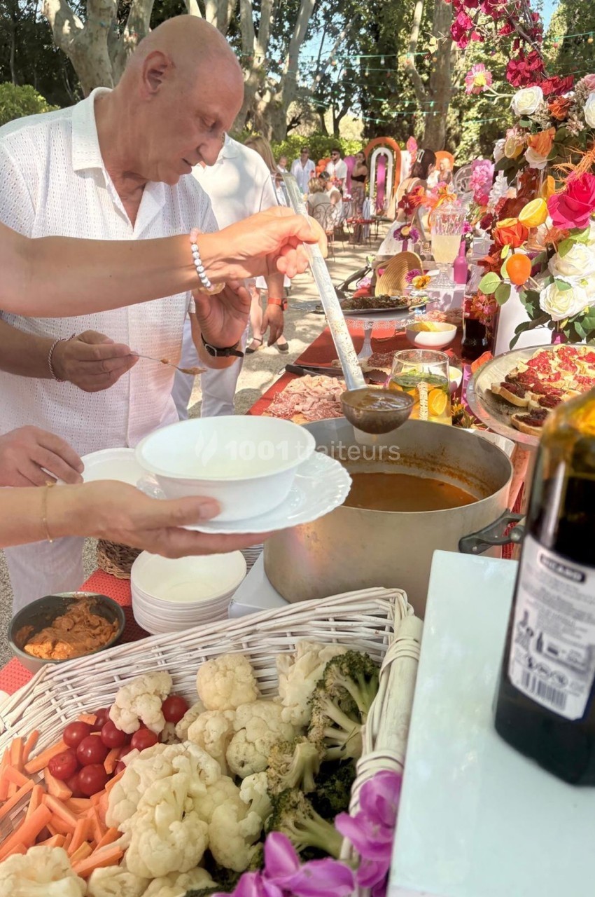 Un homme sert de la soupe dans des bols lors d'un buffet en plein air, entouré de légumes et de décorations florales.