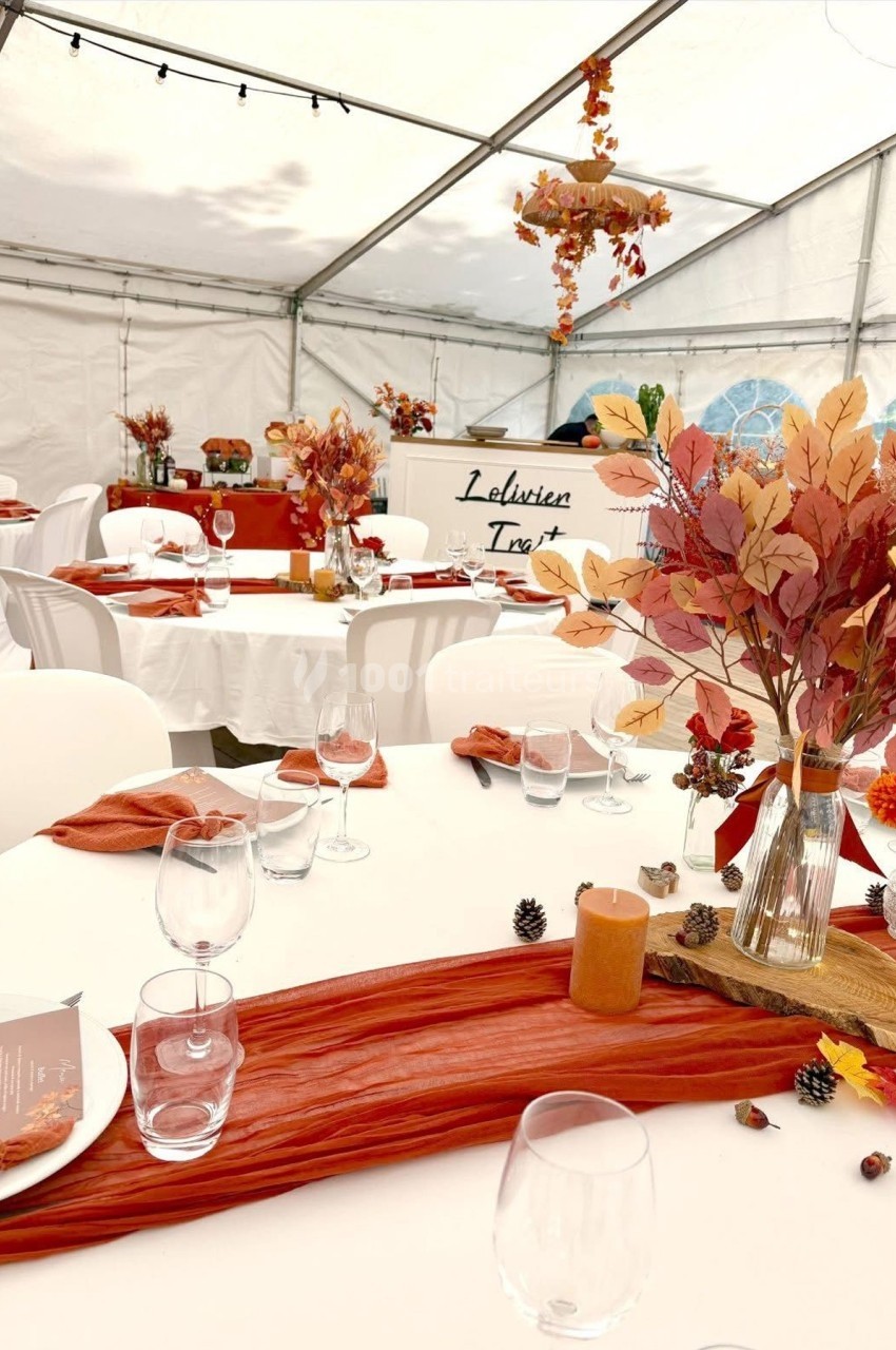 Tables décorées dans une tente, ornées de feuilles d'automne, bougies et nappes rouges pour un événement festif.