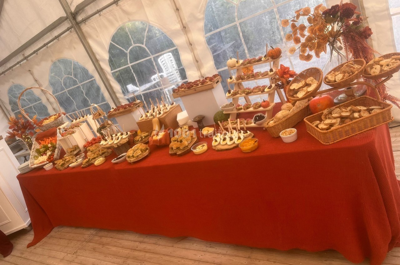 Table garnie de plats variés, notamment des desserts et des amuse-bouches, dans un décor de tente lumineuse.