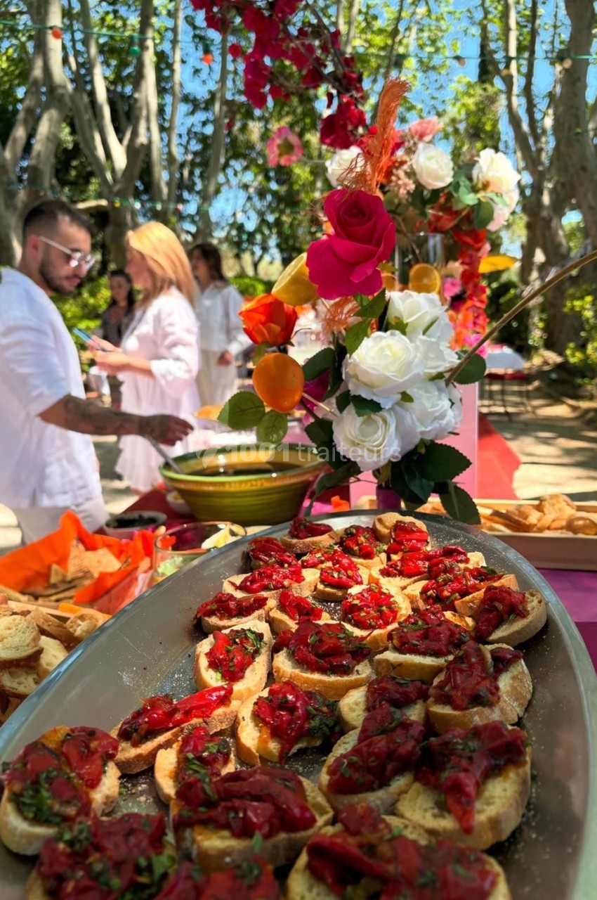 Plateau de bruschettas garnies de tomates et herbes fraîches, avec un décor floral en arrière-plan dans un jardin.