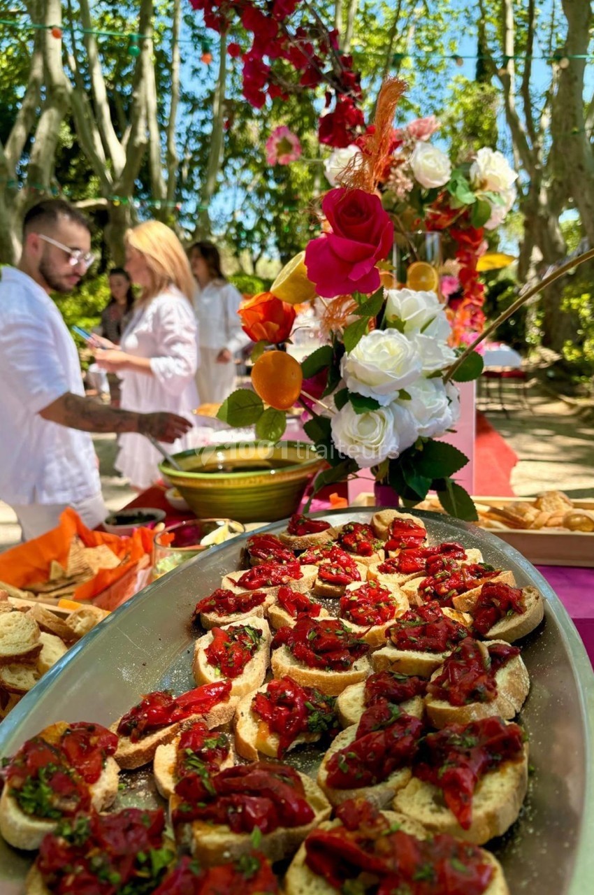 Plateau de bruschettas garnies de tomates et herbes fraîches, avec un buffet coloré en arrière-plan dans un jardin.