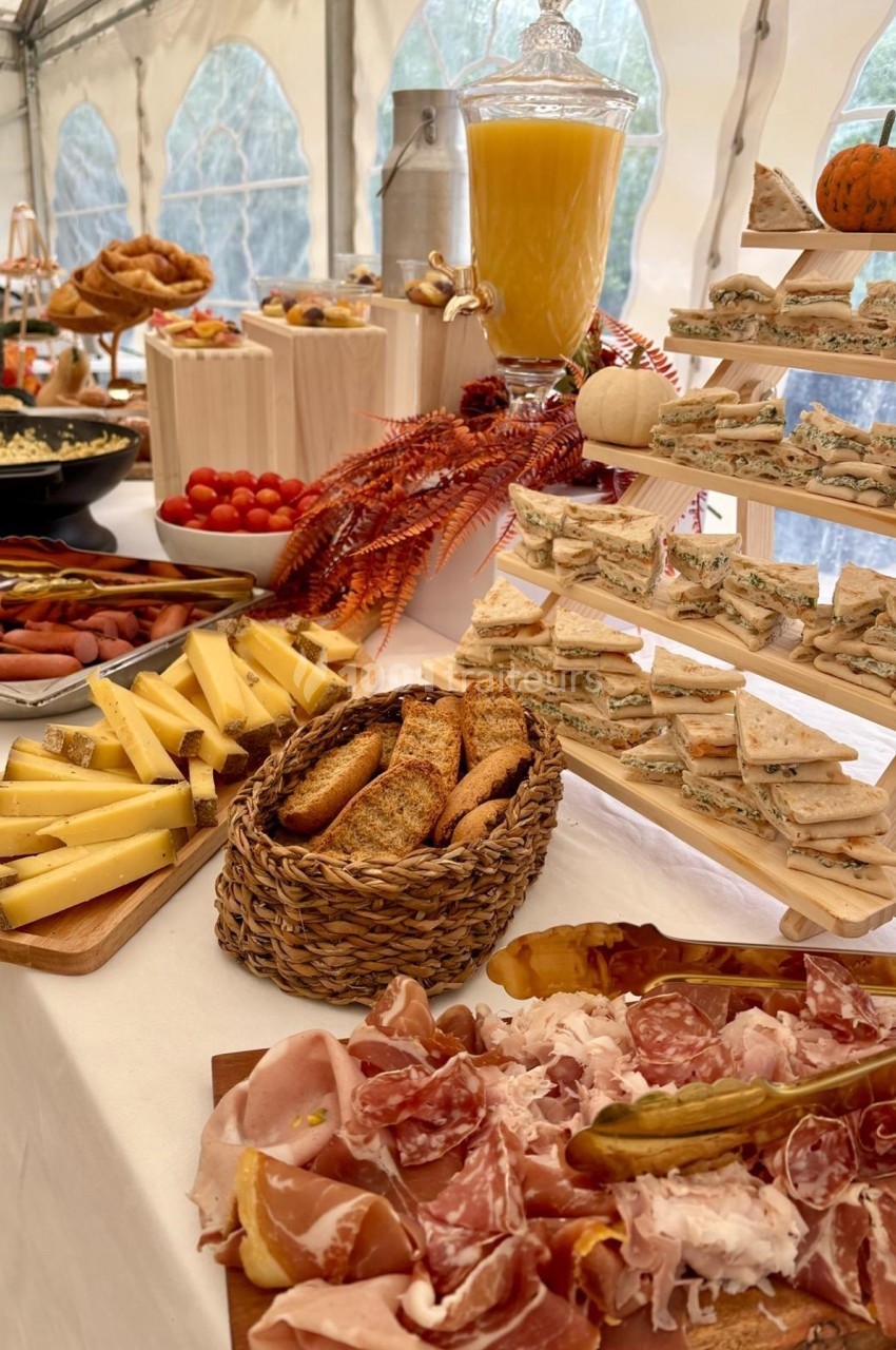 Buffet varié avec charcuterie, fromages, pains, sandwichs et jus d'orange, disposé sur une table décorée.