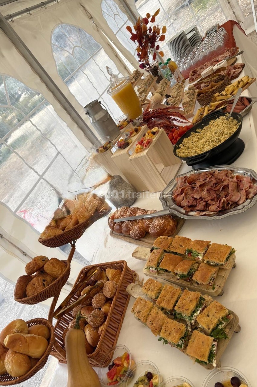 Buffet varié sous une tente, avec pains, viennoiseries, charcuterie, salades, desserts et boissons.