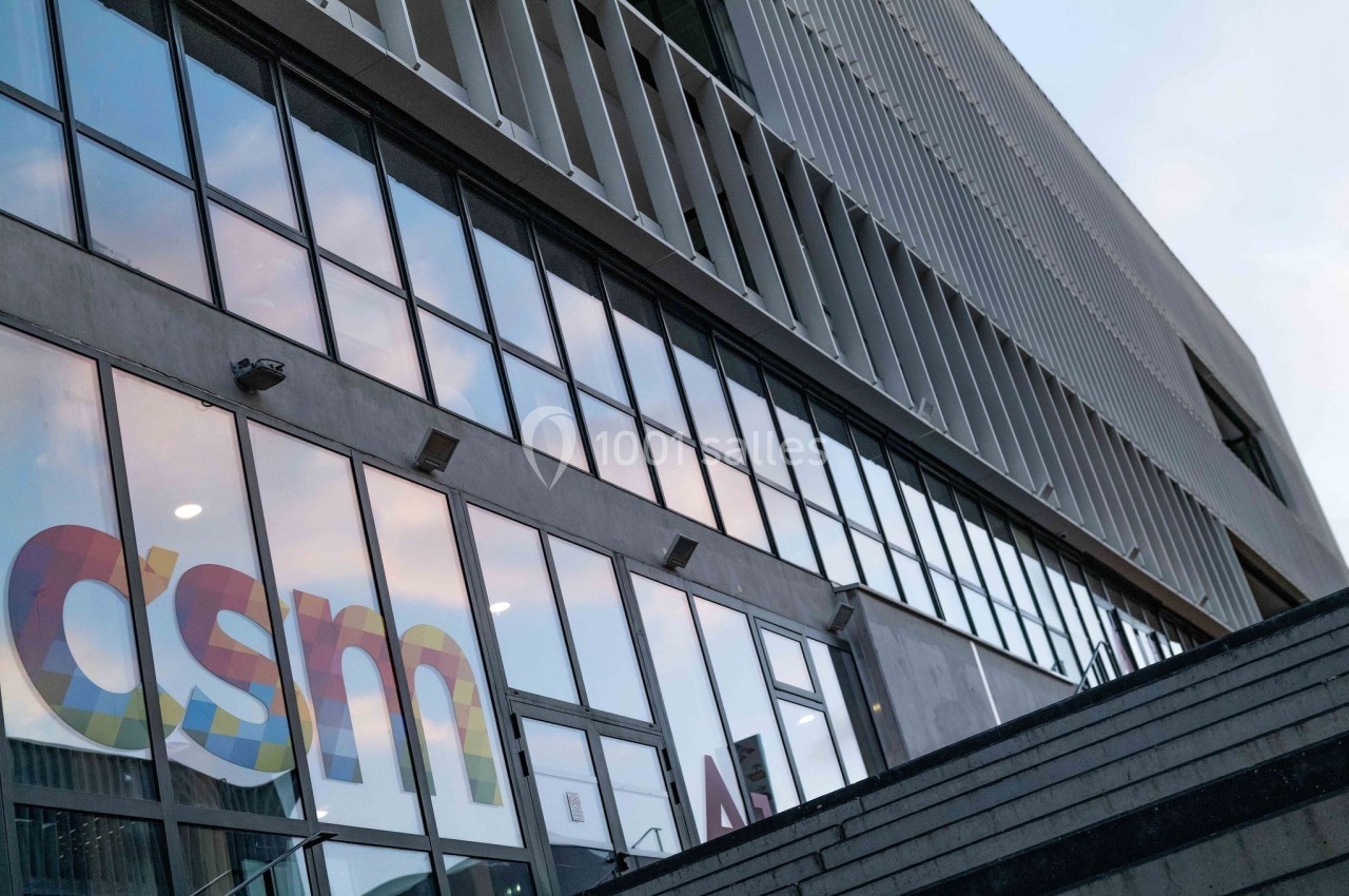 Location salle Nice (Alpes-Maritimes) - Campus Sud des Métiers #9 Façade moderne d'un bâtiment avec de grandes baies vitrées reflétant le ciel, et un logo coloré visible sur une vitre.