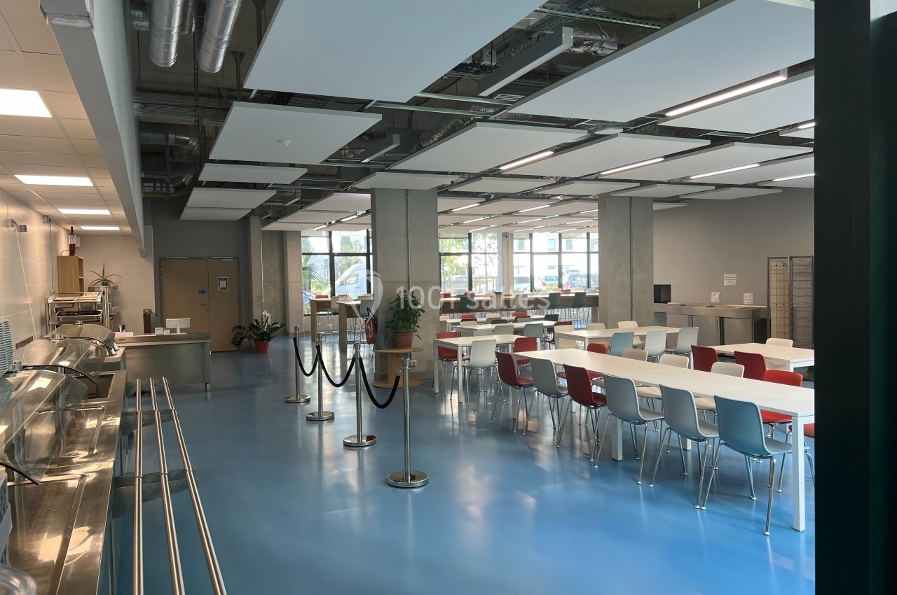 Location salle Nice (Alpes-Maritimes) - Campus Sud des Métiers #6 Salle de restauration lumineuse avec tables et chaises colorées, sol bleu et grandes fenêtres donnant sur l'extérieur.