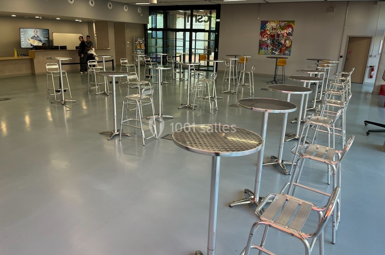 Location salle Nice (Alpes-Maritimes) - Campus Sud des Métiers #8 Salle lumineuse avec tables hautes et tabourets métalliques, comptoir d'accueil et tableau coloré en arrière-plan.