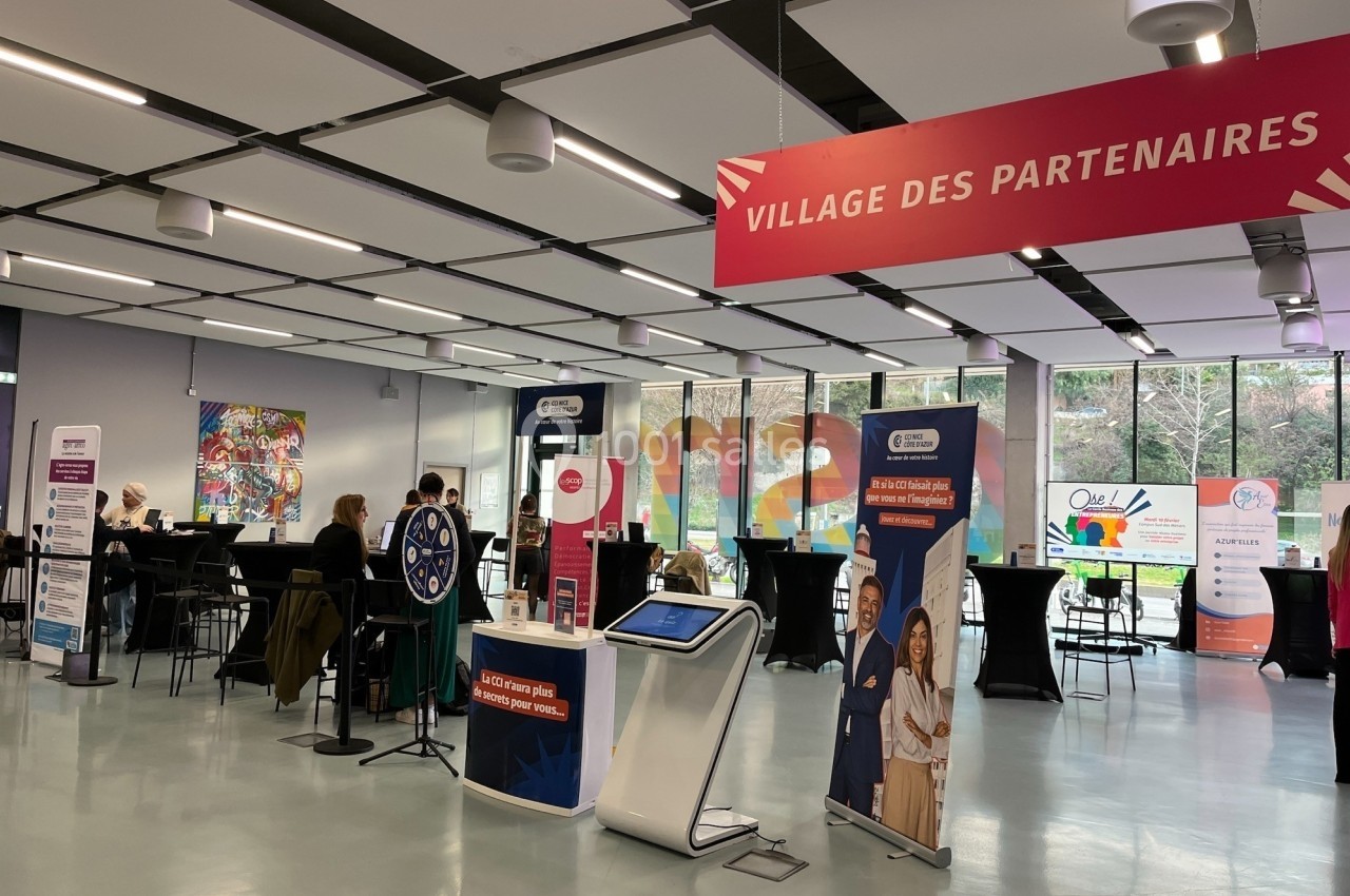 Location salle Nice (Alpes-Maritimes) - Campus Sud des Métiers #5 Espace intérieur avec des stands d'information sous une bannière ’Village des partenaires’, quelques personnes présentes.