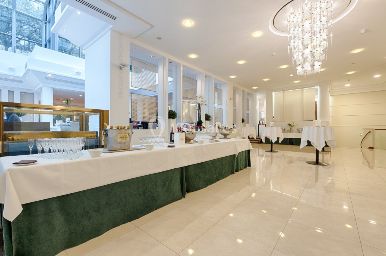 Salle lumineuse avec tables dressées pour un buffet, décor moderne et grand lustre au plafond.