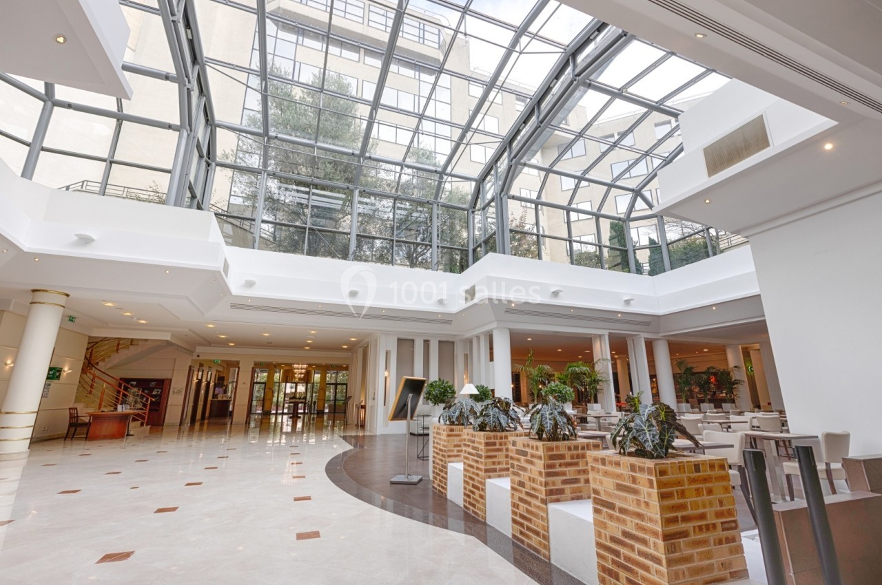 Intérieur d'un hall spacieux avec verrière, plantes décoratives et sol en marbre clair.