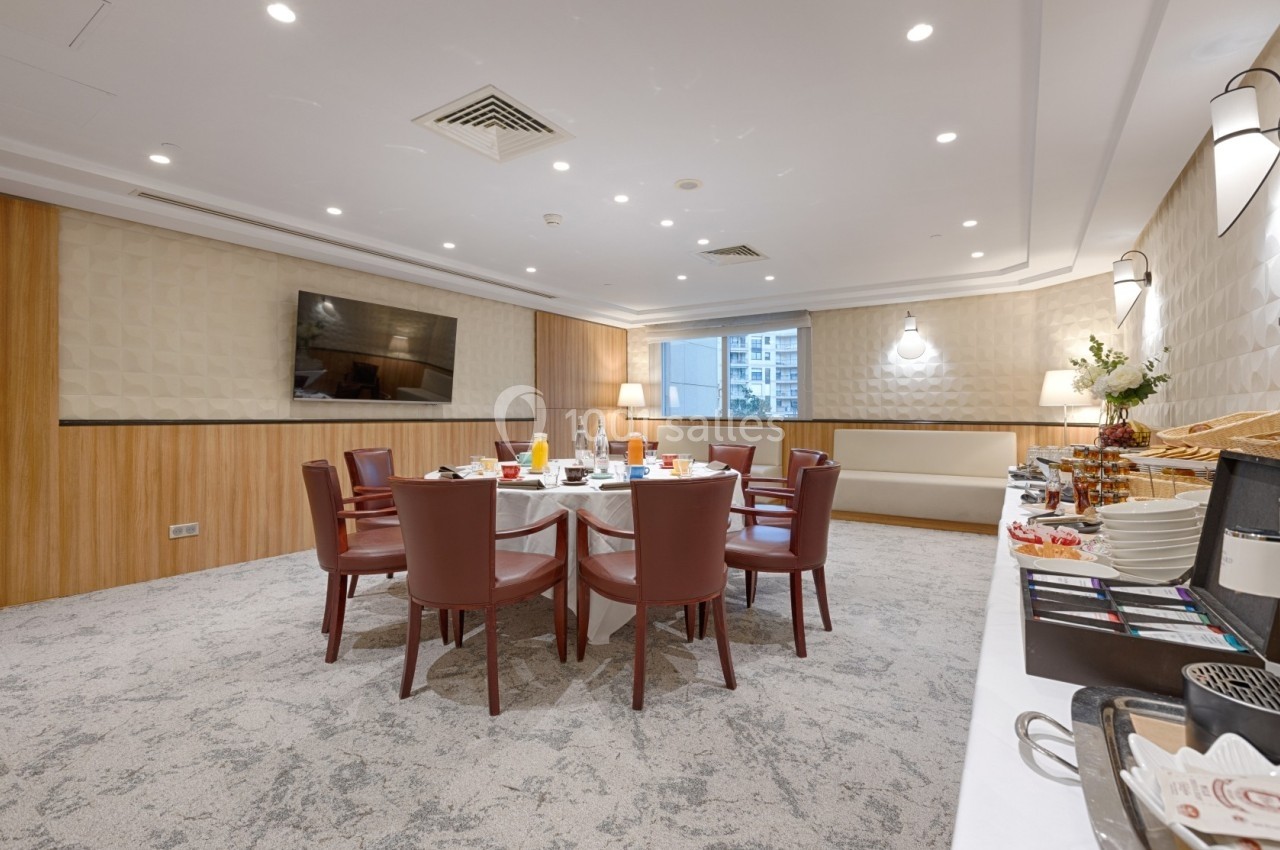 Salle de réunion avec table dressée pour un petit-déjeuner, entourée de chaises, buffet en arrière-plan.