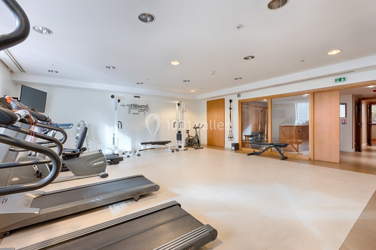 Salle de sport lumineuse avec tapis de course, machines de musculation, vélo d'exercice et banc de musculation.