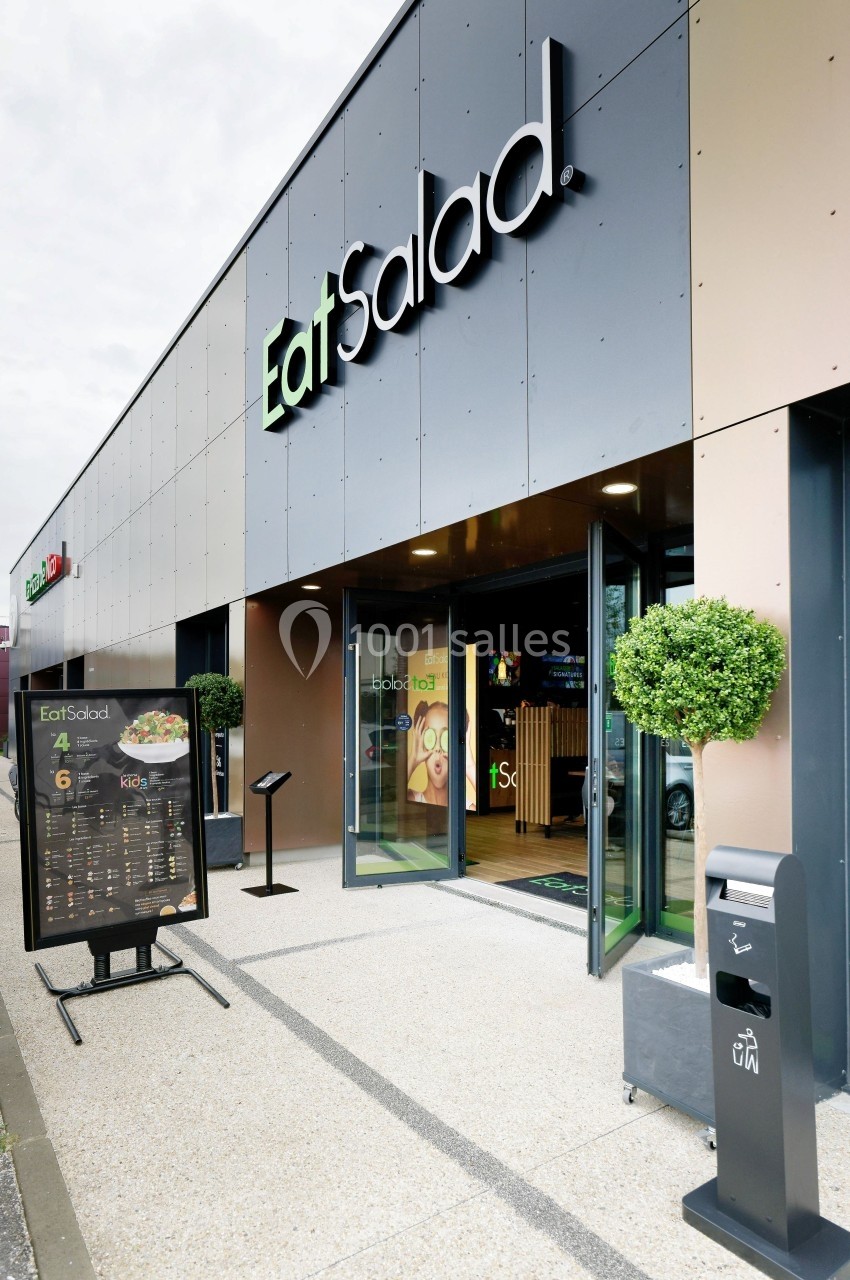 Façade d'un restaurant avec enseigne ’Eat Salad’, entrée vitrée, menu extérieur et poubelle à proximité.