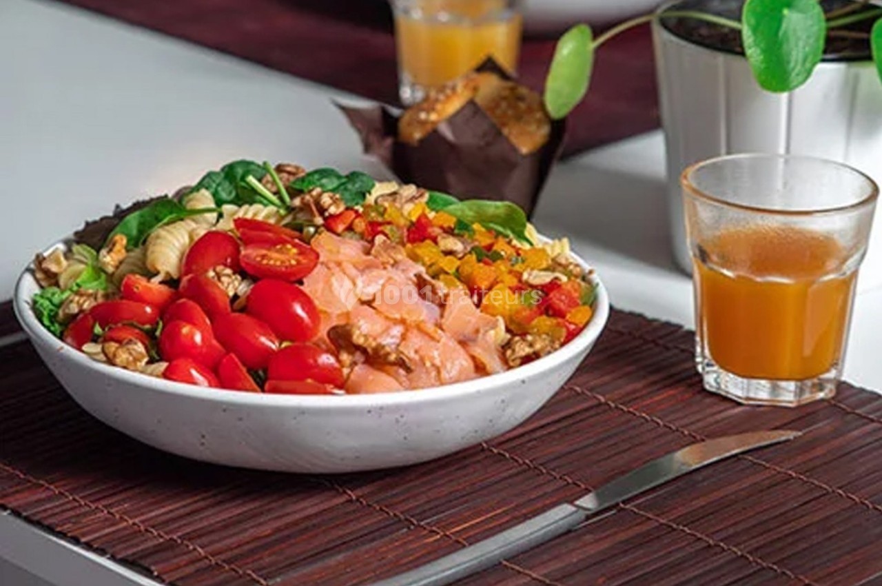 Bol de salade composé de légumes frais, saumon, noix et fruits secs, accompagné d'un verre de jus et d'un muffin.