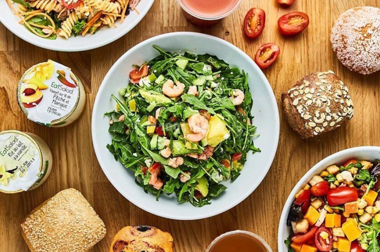 Assortiment de plats et aliments variés sur une table en bois, incluant salade, pain, fruits et boissons.