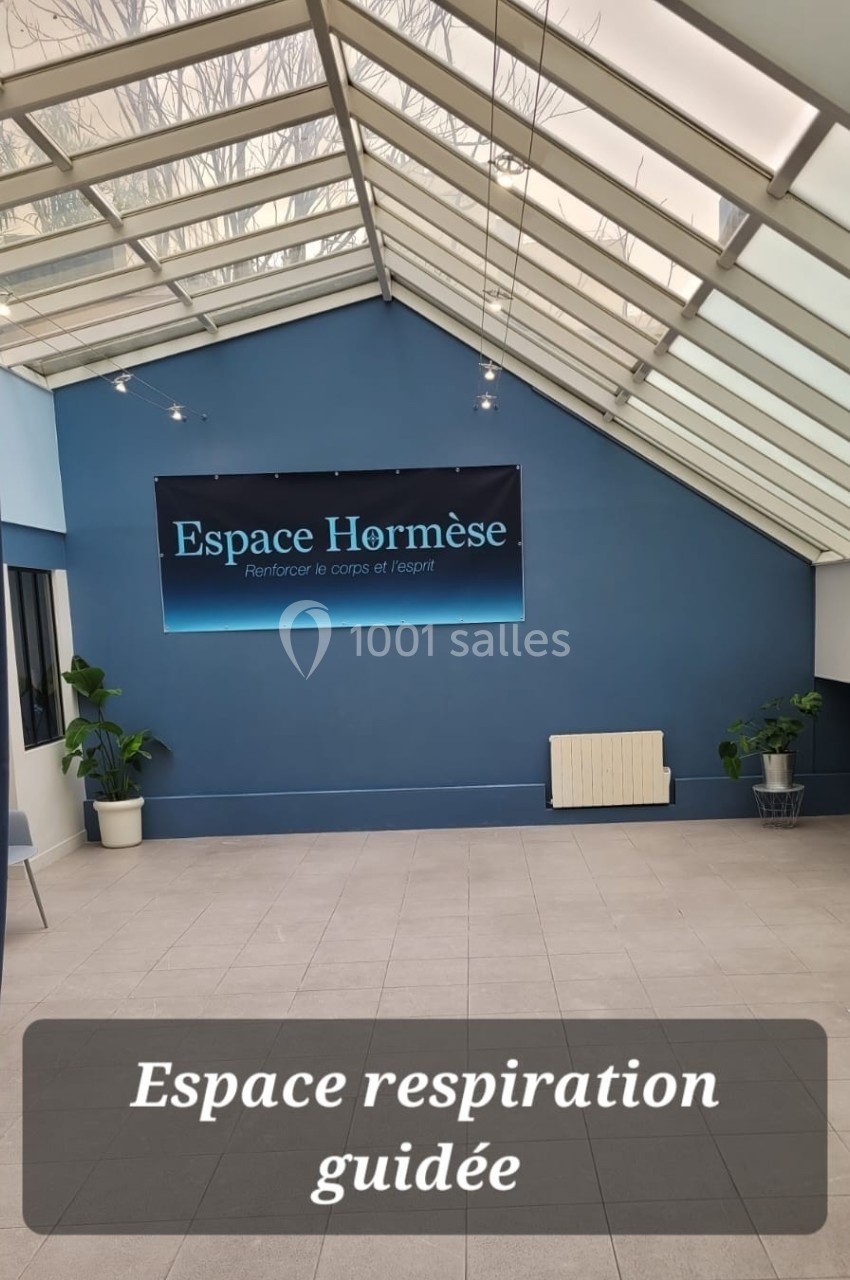 Salle lumineuse avec verrière, murs bleus, plantes et panneau ’Espace Hormèse’ sur le mur du fond.