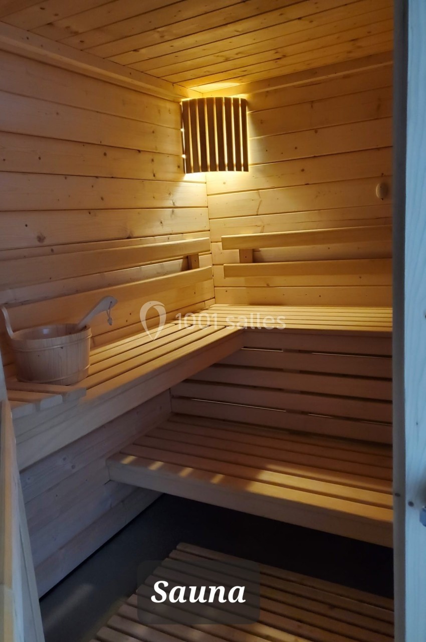 Intérieur d'un sauna en bois clair avec bancs, seau en bois et lumière douce.