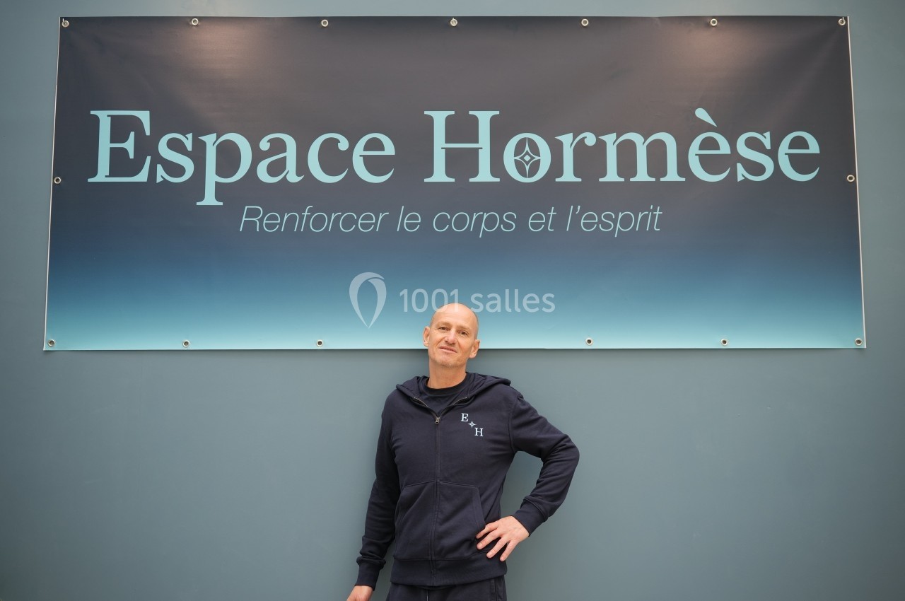 Un homme en tenue sportive pose devant une affiche indiquant ’Espace Hormèse, Renforcer le corps et l'esprit’.