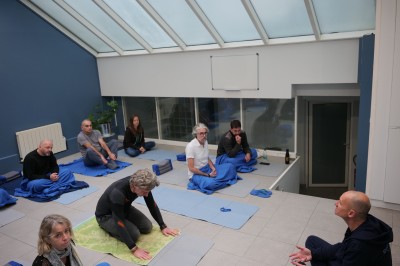 Des personnes assises sur des tapis dans une salle lumineuse, participant à une séance de méditation ou de discussion.