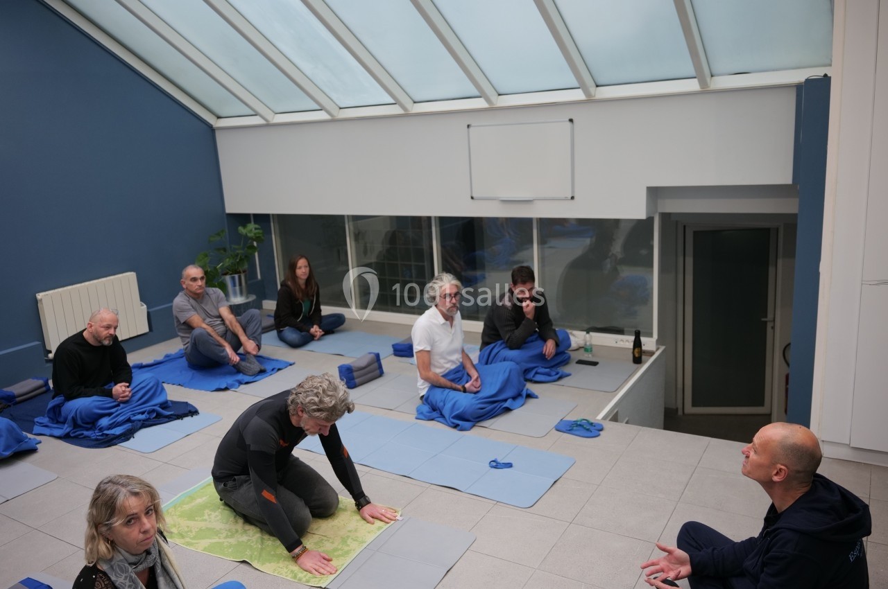 Des personnes assises sur des tapis dans une salle lumineuse, participant à une séance de méditation ou de discussion.