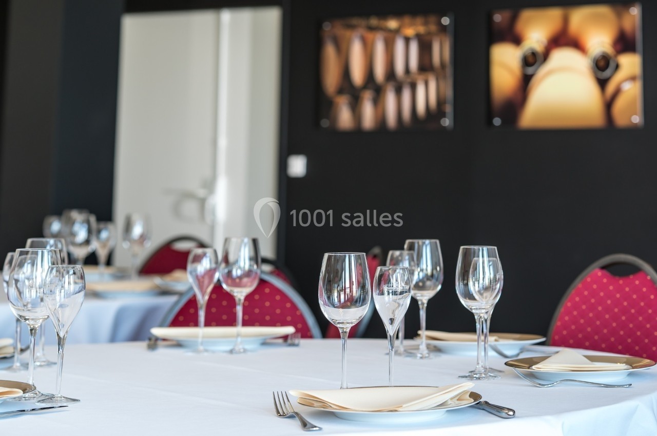 Salle de restaurant élégante avec tables dressées, nappes blanches, verres à vin et assiettes, décor sobre en arrière-plan.