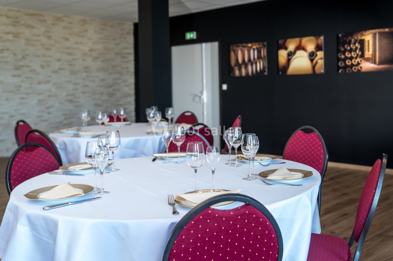 Salle de réception avec tables rondes dressées, nappes blanches, chaises rouges et décorations murales modernes.