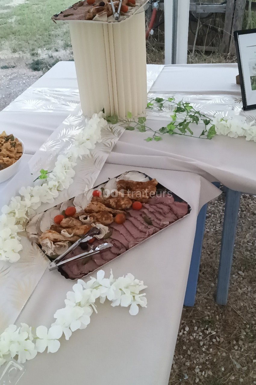 Plateau de viandes grillées et tranchées avec tomates cerises, présenté sur une table décorée de fleurs blanches.