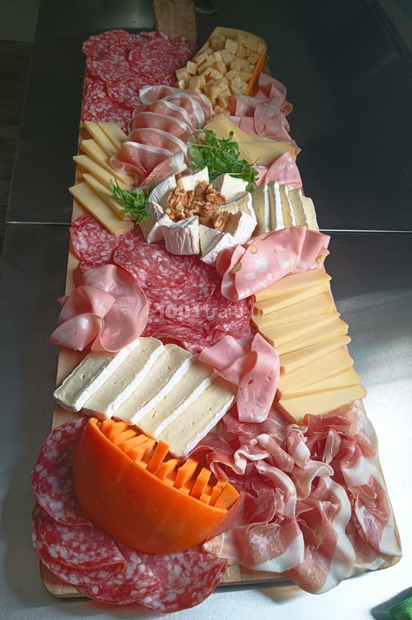 Plateau de charcuteries et fromages variés disposés sur une planche en bois, avec quelques feuilles de roquette.