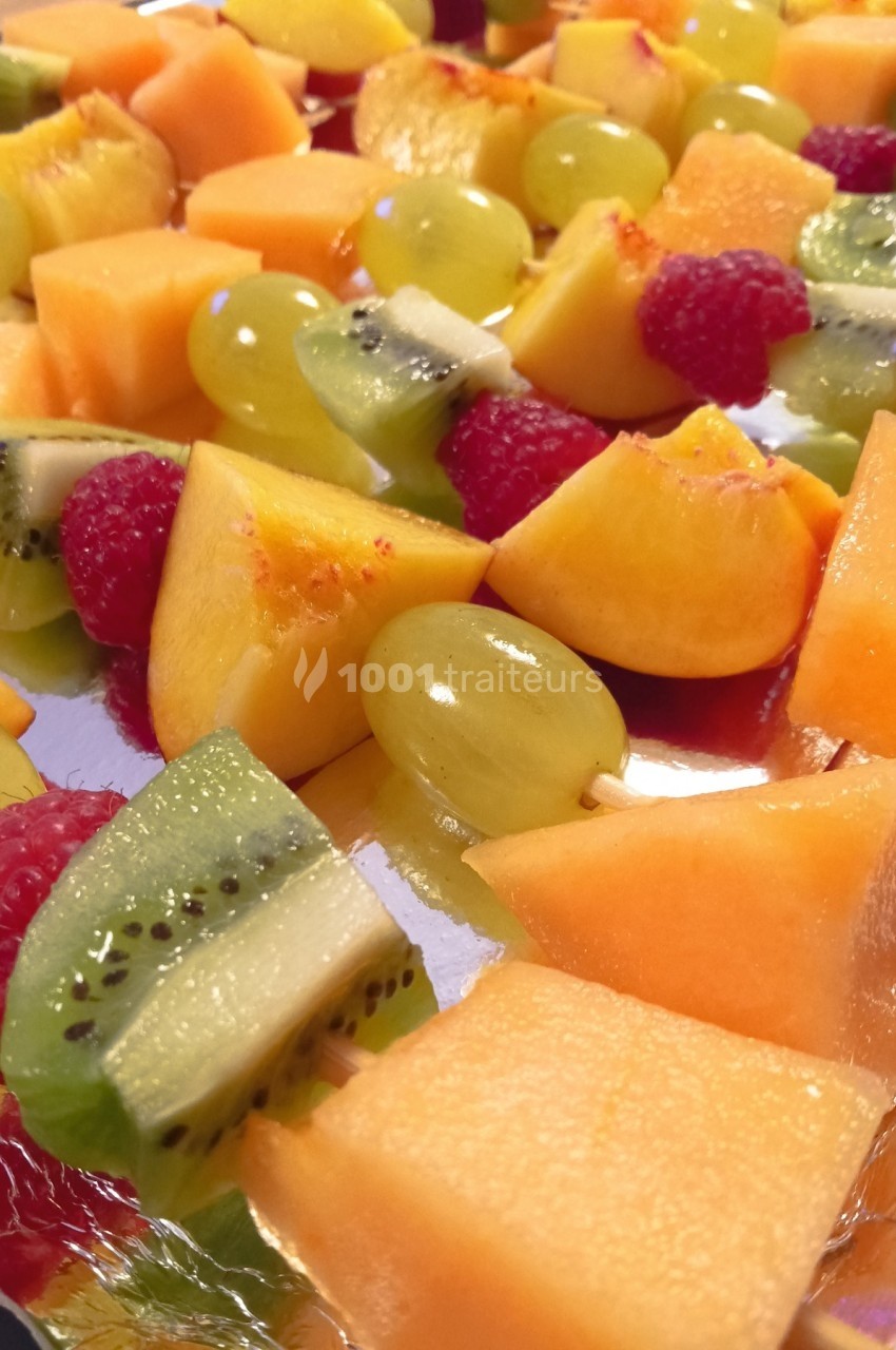 Assortiment de brochettes de fruits frais comprenant melon, kiwi, raisin, framboise et pêche sur un plateau.