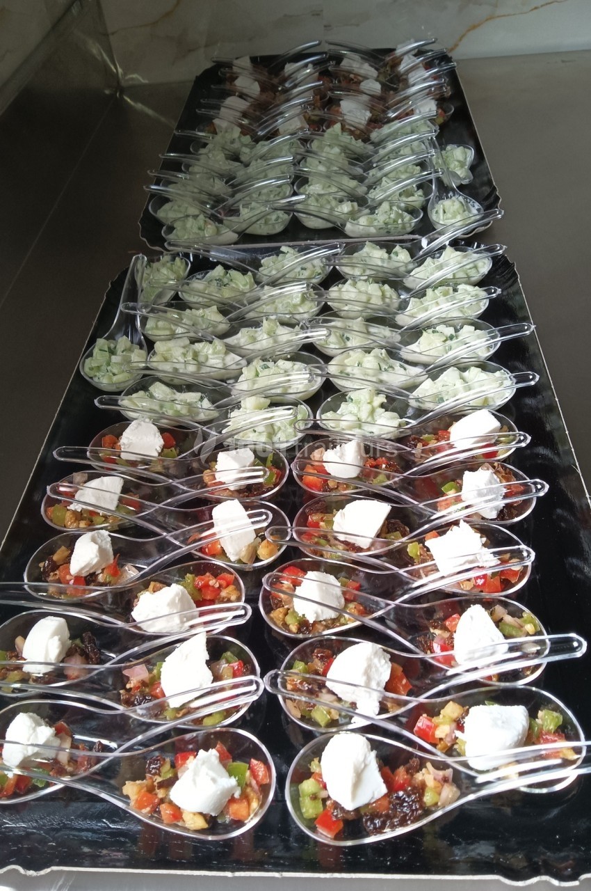 Cuillères apéritives alignées, garnies de légumes colorés, fromage frais et dés de concombre sur un plateau noir.