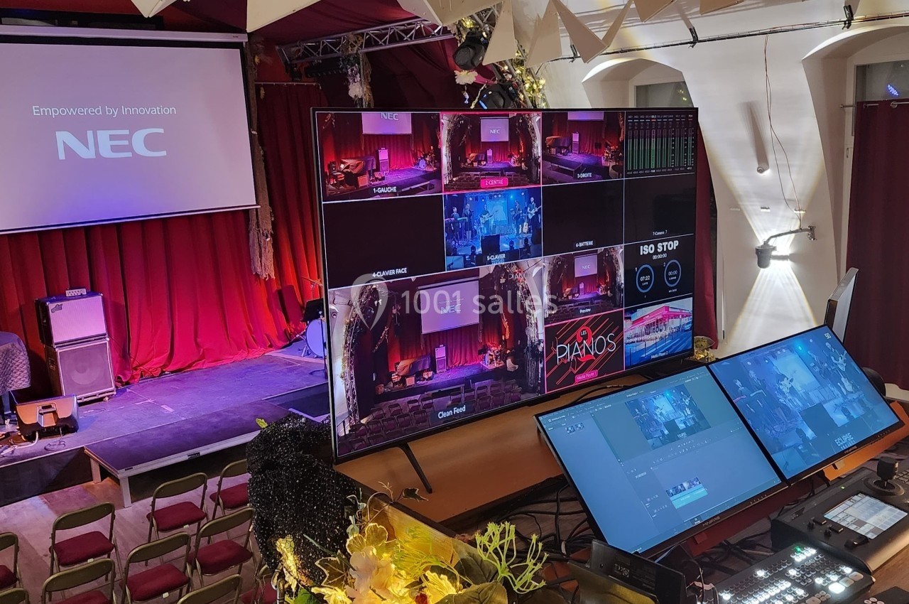 Salle de spectacle équipée de matériel audiovisuel, avec écrans de contrôle et scène en arrière-plan.
