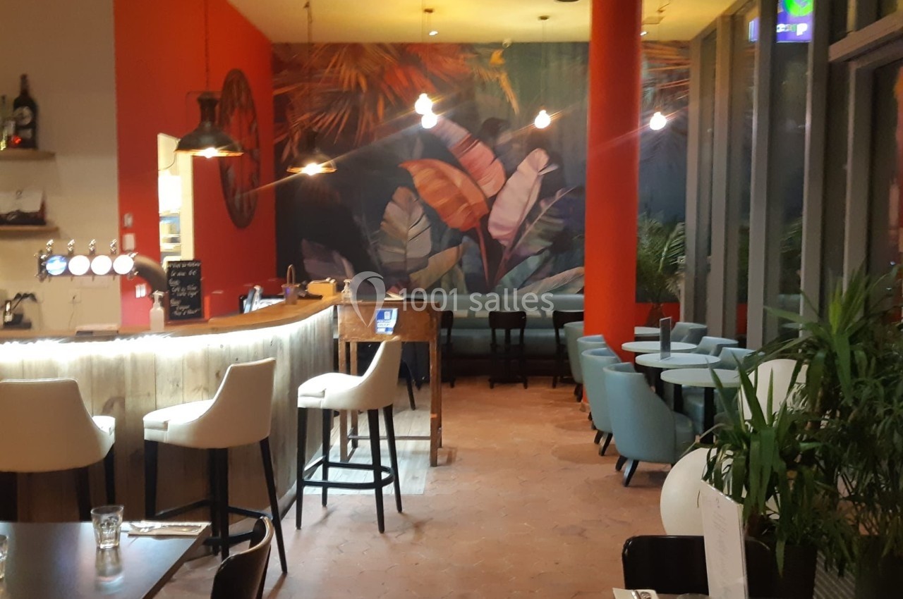 Intérieur d'un restaurant avec un bar, des tables, des chaises modernes et une fresque murale tropicale colorée.