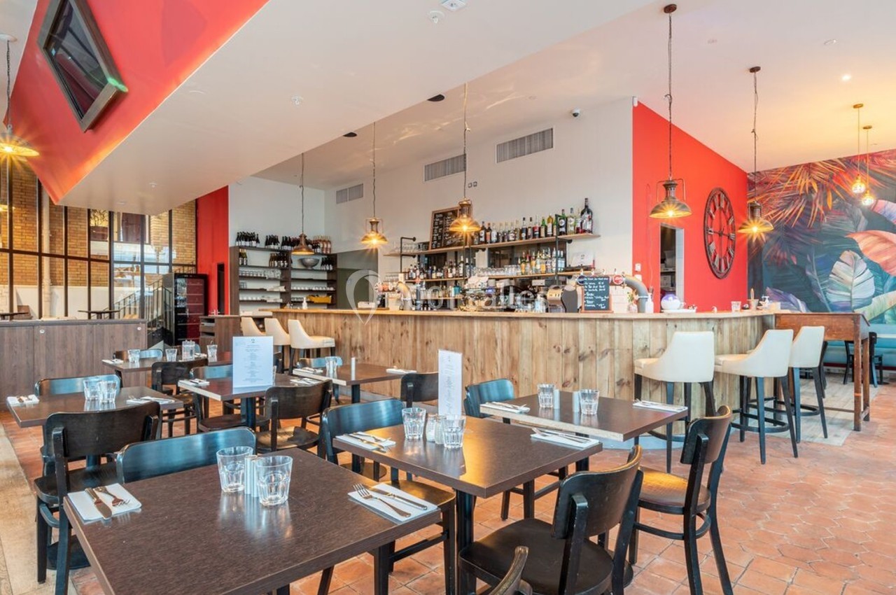 Salle de restaurant moderne avec tables dressées, bar en bois, murs rouges et fresque colorée en arrière-plan.