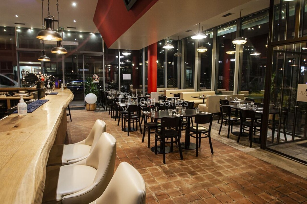Salle de restaurant moderne avec bar en bois, tables dressées et grandes baies vitrées donnant sur l'extérieur.