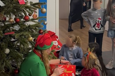 Une femme surveille deux jeunes enfants jouant avec des jouets dans un bac à sable en plein air.