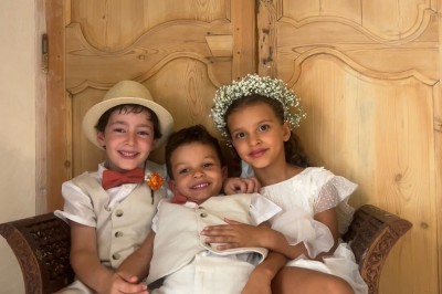 Panneau ’Kids Area’ en bois près d'une aire de jeux, avec une femme de dos portant un t-shirt ’Babysitting’.