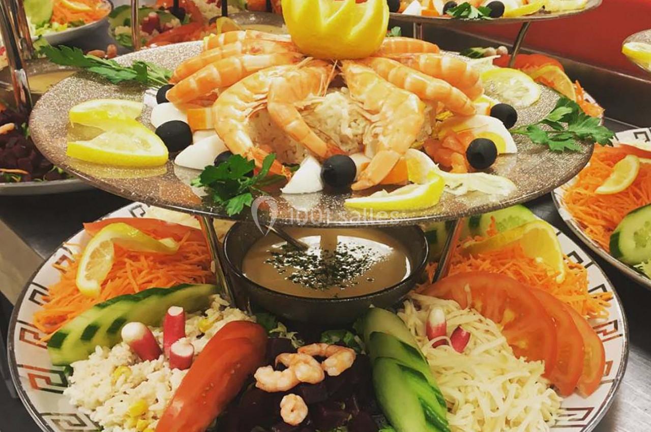 Plateau de fruits de mer avec crevettes, légumes frais, citron et sauce, présenté sur un support décoratif.
