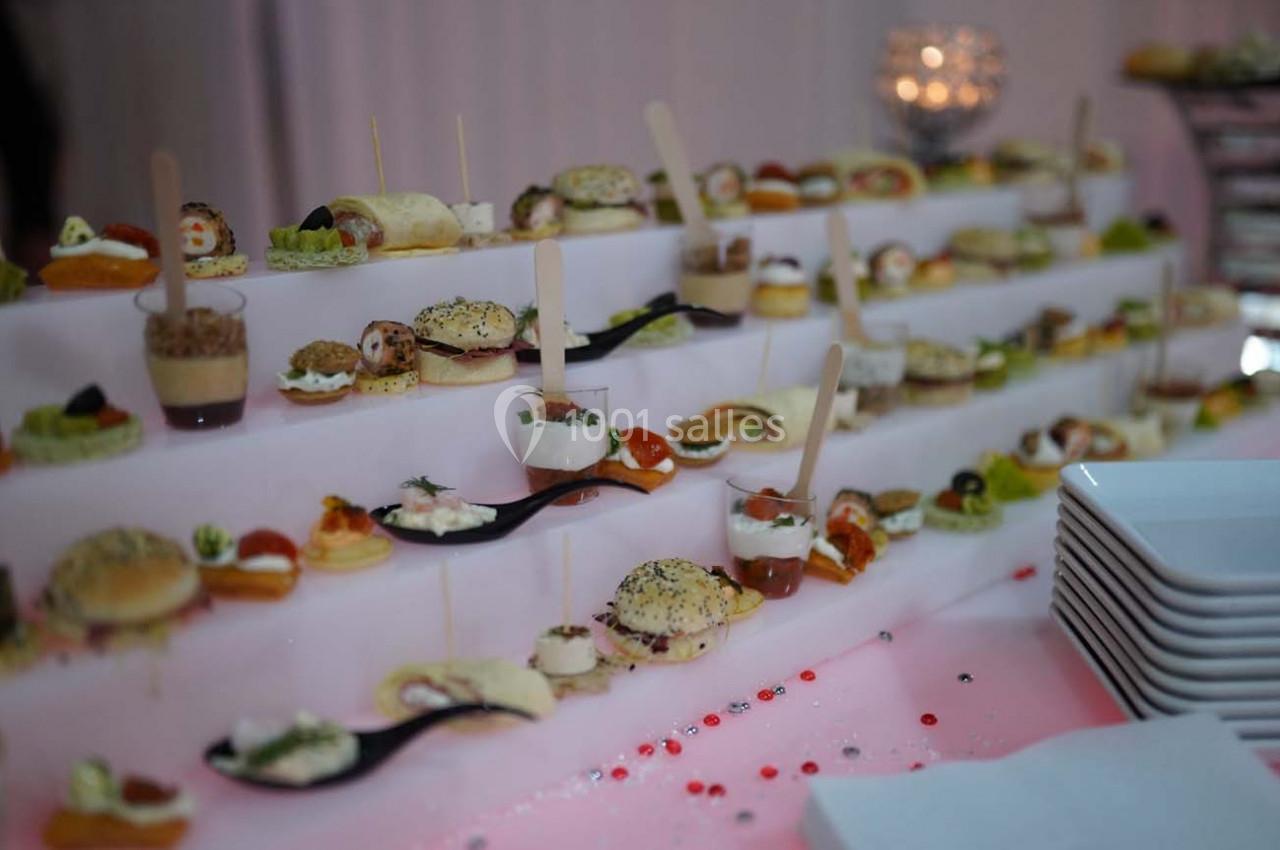 Plateau de bouchées apéritives variées présentées sur des étagères, avec des assiettes empilées à droite.