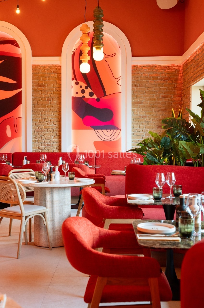 Salle de restaurant moderne avec murs en briques, décorations colorées, plantes et tables dressées.