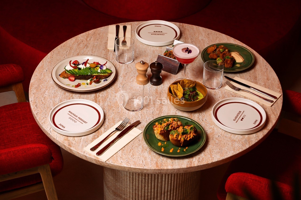 Table dressée avec des assiettes garnies de plats variés, couverts, verres et condiments sur une table ronde en marbre.