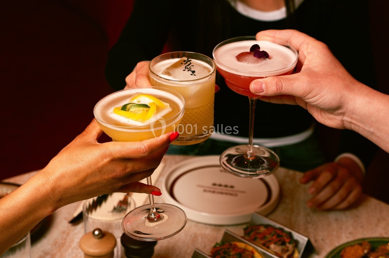 Trois personnes trinquent avec des cocktails variés autour d'une table garnie de plats.