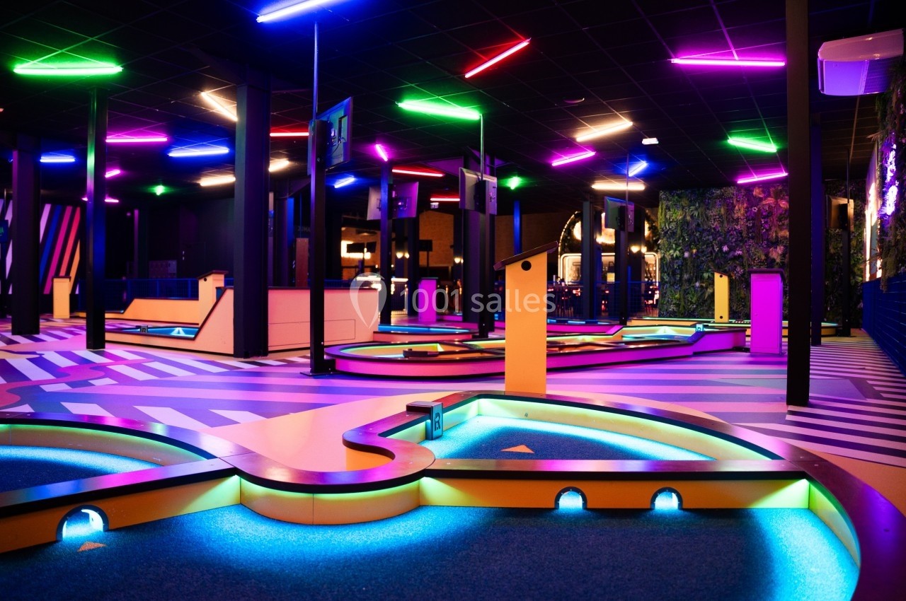 Parcours de mini-golf intérieur avec éclairage néon coloré et décorations modernes.