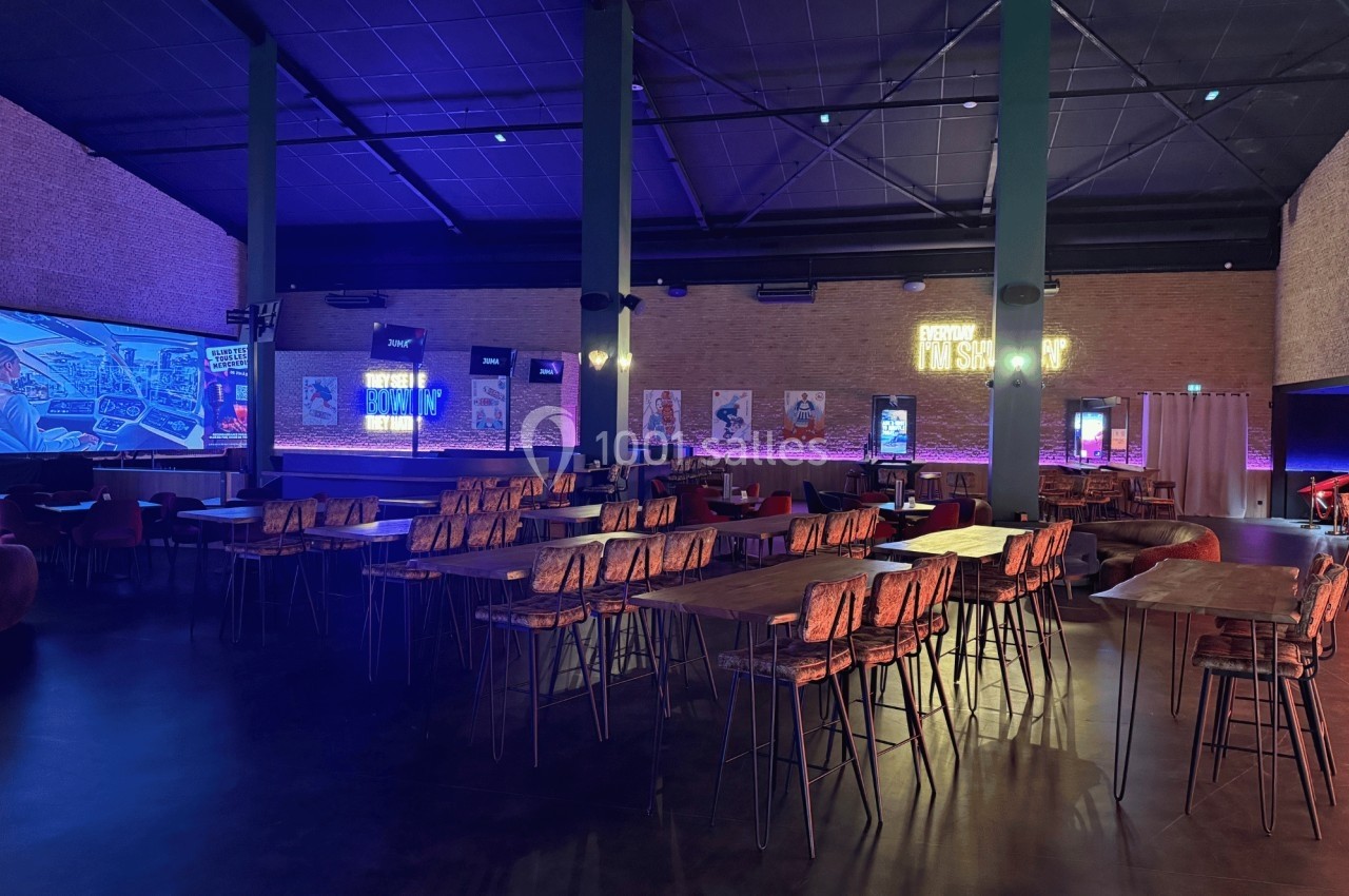 Salle spacieuse avec tables et chaises en bois, éclairage tamisé et néons colorés sur les murs en briques.