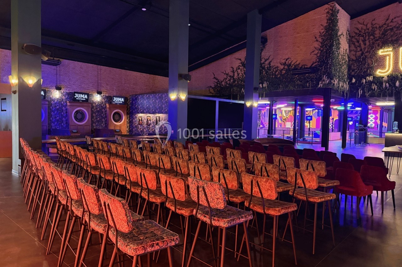 Salle aménagée avec des rangées de chaises face à une scène, éclairée par des lumières tamisées et colorées.