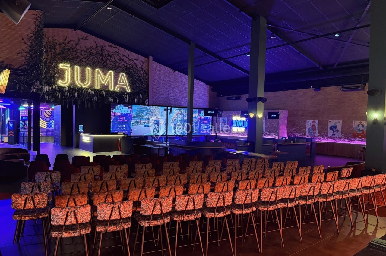Salle aménagée avec des rangées de chaises face à une scène éclairée, dans un espace moderne et coloré.