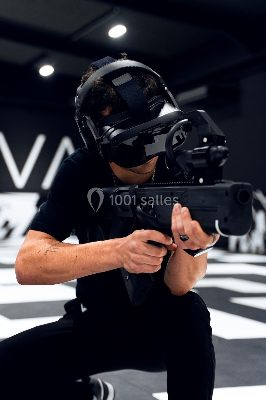 Homme portant un casque de réalité virtuelle et tenant un équipement simulant une arme dans un environnement intérieur.