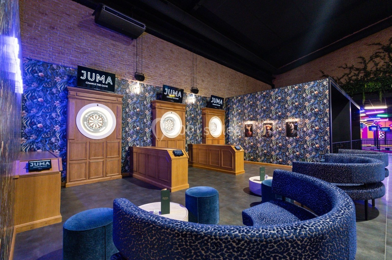 Salle de jeux avec cibles de fléchettes lumineuses, fauteuils bleus et décorations murales à motifs floraux.