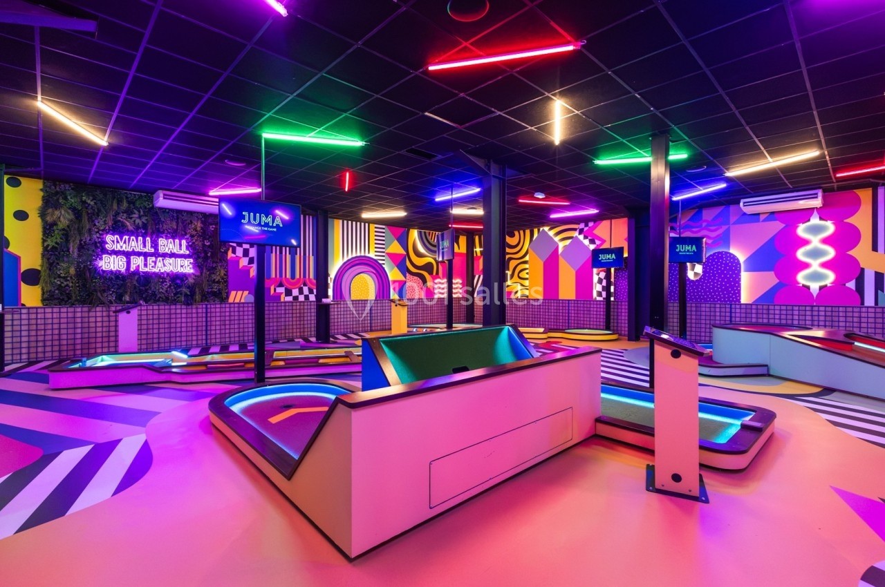 Salle de mini-golf intérieure colorée avec éclairage néon, décorations géométriques et ambiance rétro.