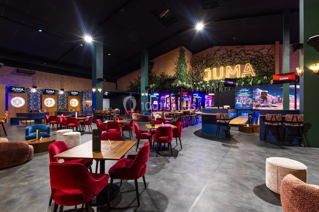 Salle moderne avec tables, chaises colorées, éclairage tamisé et enseigne lumineuse ’JUMA’ sur un mur végétalisé.