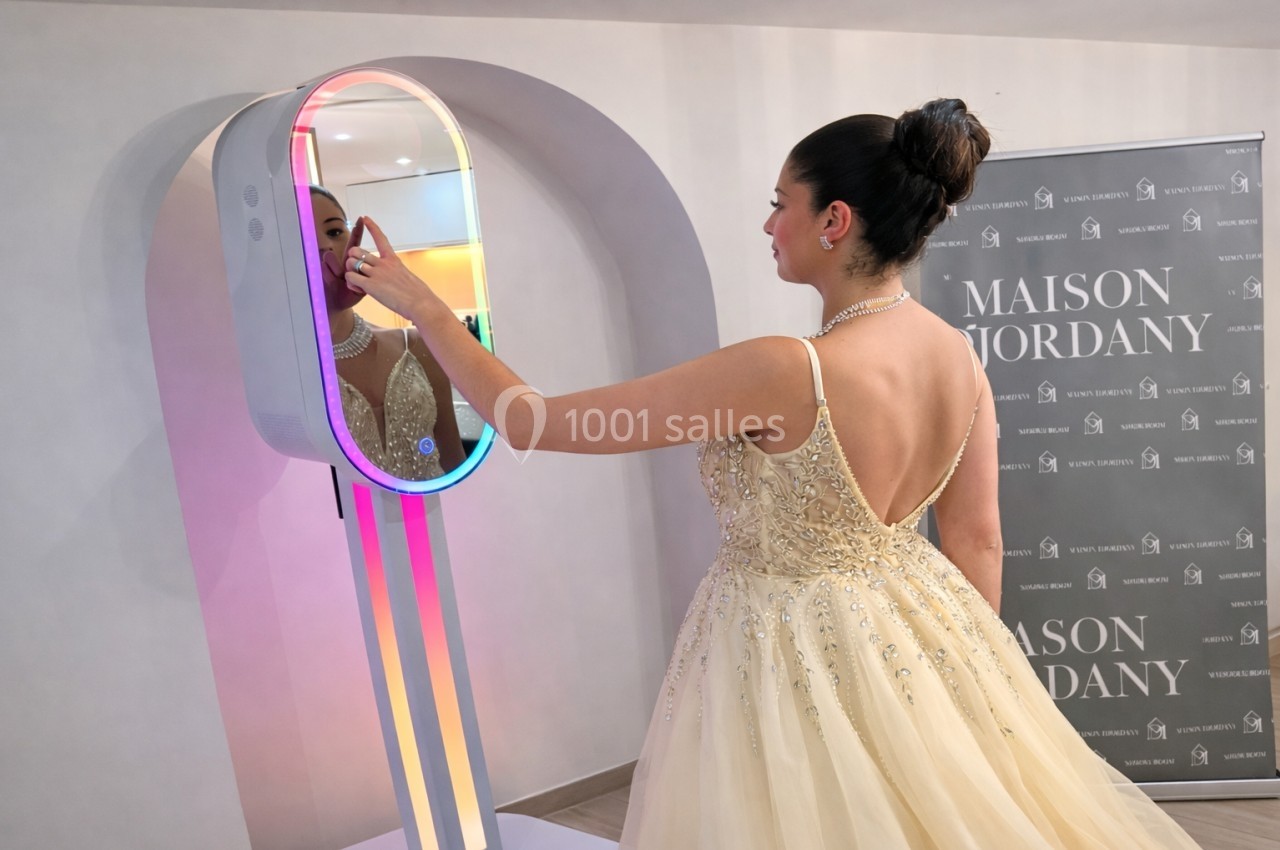 Une femme en robe de soirée beige interagit avec un miroir lumineux dans un espace intérieur.