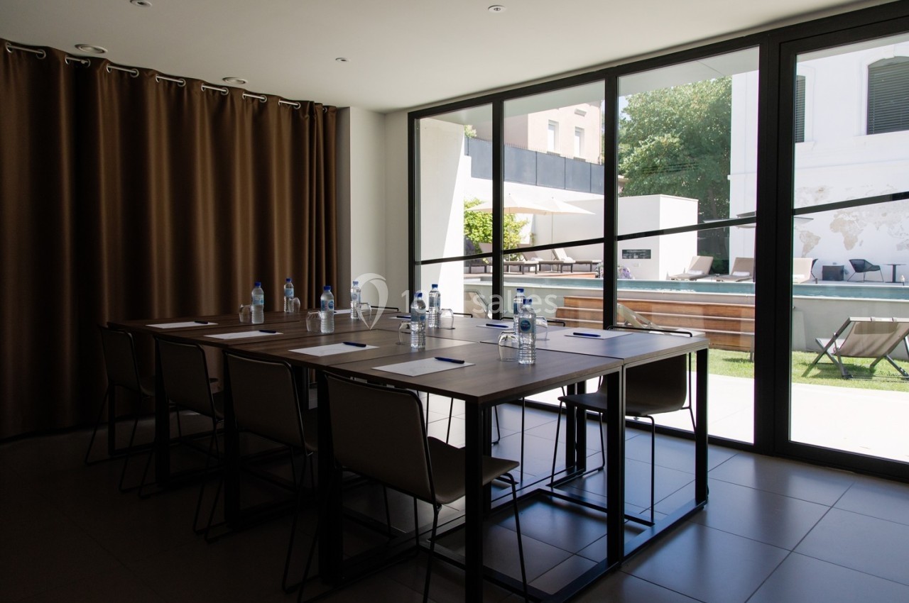 Salle de réunion lumineuse avec une grande table, des chaises, des bouteilles d'eau et vue sur une terrasse extérieure.